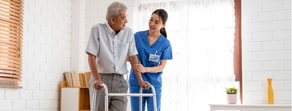 A healthcare worker in blue scrubs assists an elderly man using a walker, highlighting hybrid care by medbridge.