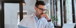 A bearded man with glasses reads a document in well-lit room, possibly reviewing Medbridge strategies.