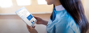 A person in a blue shirt interacts with Medbridge software on a white tablet in a softly lit room.
