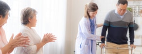 A man with a walker receives assistance from a medical professional, with two women clapping in encouragement, highlighting modern Medbridge care.