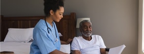 A healthcare worker and an elderly man in a wheelchair use Medbridge software to review a document together.