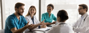 Five healthcare professionals discuss around a table with a city view, reflecting medbridge's collaborative spirit.