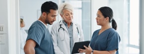 Three medical professionals discuss Medbridge software on a tablet in a hospital corridor.