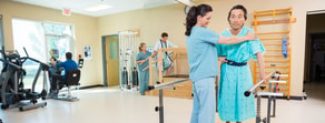 A physical therapist helps a patient in a hospital rehab gym while others use equipment, as seen on the medbridge platform.