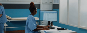 A healthcare professional in blue scrubs uses a computer in a hybrid care setting with medbridge.