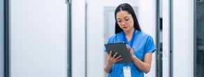 A healthcare professional in scrubs uses a tablet with medbridge software in a corridor.