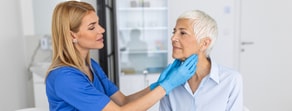 A nurse in blue scrubs examines an older woman's neck using medbridge software.
