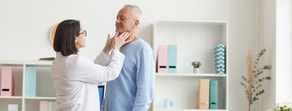 An expert examines an elderly man's neck in a well-lit office with medbridge solutions visible.