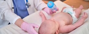 A healthcare professional feeds a baby from a bottle on an examination table, highlighting the role of Medbridge in enhancing pediatric care.