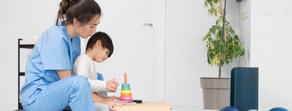 A healthcare worker helps a child with a stacking toy, showcasing Medbridge's hands-on education.