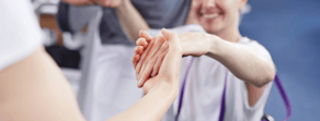 A smiling wheelchair user extends their hand to another person, who is reaching back, in a medbridge ad.