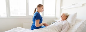 A nurse in blue scrubs holds the hand of a smiling elderly patient in a bright hospital room, symbolizing compassionate care at medbridge.