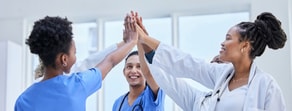 Medical professionals in scrubs and coats high-five, capturing Medbridge's healthcare training spirit.