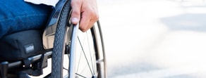 Hand on a wheelchair wheel, outdoors in the background.
