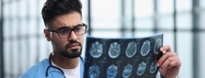 A doctor in a blue coat examines a brain MRI scan at a well-lit Medbridge facility.