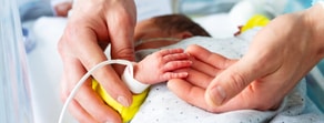 A newborn's hand with a vital monitor band in an adult's hand from medbridge.