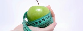 A hand holds a green apple wrapped with a blue measuring tape on a plain white background.