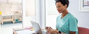 A healthcare professional in scrubs uses a laptop in a bright medical office to explore medbridge patient care software.