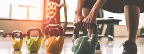 A person lifts a green kettlebell in a gym with medbridge branding.