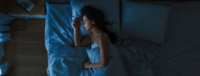 A woman sleeps on her side under a blue blanket, illustrating the importance of rest in medbridge health.