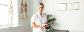 A woman in a white lab coat smiles in a medical office, representing healthcare training with medbridge.