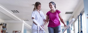 A healthcare professional uses medbridge software to help a woman walk on parallel bars in rehab.