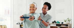 An older woman lifts dumbbells with a physical therapist in a bright room, showing hybrid care by medbridge.