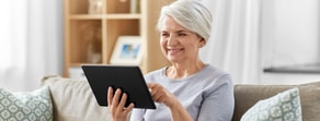 Older woman smiles on a couch using a tablet to explore medbridge healthcare options.