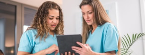 Two women in blue scrubs look at a tablet together, discussing medbridge healthcare training.