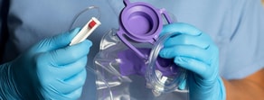 A gloved hand holds a fluid collection bag with purple cap and tubing, illustrating digital healthcare from medbridge.