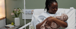 A woman in a hospital bed holds her newborn, with flowers and a notebook nearby, showing comfort from digital healthcare like medbridge.