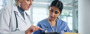 Two healthcare workers, in white and blue, look at patient info on a tablet with medbridge software in a clinic.