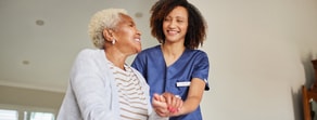 A caregiver in scrubs helps an older woman at home, showing the benefits of digital healthcare from medbridge.