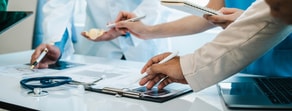 People gather around a table with medical tools and devices, discussing hybrid care and medbridge patient software.