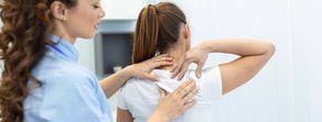 A healthcare professional examines a woman's upper back and neck in a medbridge clinical setting.
