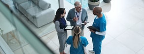 Four healthcare professionals review information on tablets and clipboards with medbridge patient care software indoors.