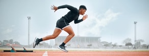 A runner sprints from starting blocks on an outdoor track under a cloudy sky, representing medbridge's drive and dedication.