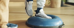 Person in athletic shoes balances on a blue half-dome balance trainer indoors during medbridge healthcare training.