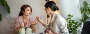 Two women on a couch discuss healthcare education, one gesturing as she speaks and the other listening, possibly about medbridge.