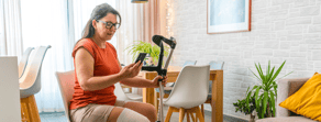 A woman with a bandaged leg sits on a couch, holding crutches and looking at her phone, possibly using medbridge.