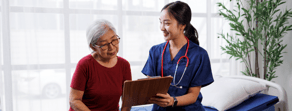 A nurse in blue scrubs discusses a clipboard with an older woman, emphasizing medbridge healthcare education.