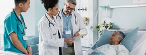 Three medical professionals use medbridge at a hospital bedside while an elderly patient watches.