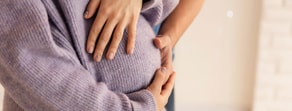 Two people embrace with hands on a pregnant belly; one wears a lavender sweater.