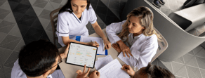 Four people in white uniforms sit at a table, one holding a tablet showing medbridge patient care software.