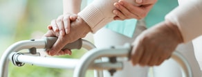 A caregiver assists an elderly person using a walker, promoting independence through hybrid care.