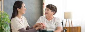A caregiver and an elderly woman in a wheelchair share a joyful moment together.