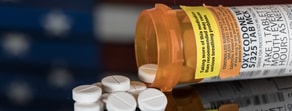 A prescription bottle and tablets on a reflective surface with a blurred American flag background represent healthcare caution in evolving digital America.