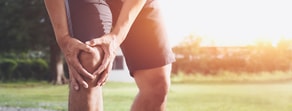 A person in shorts holds their knee outdoors, highlighting medbridge's role in pain management.