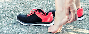 Individual holding a bare foot, with black and red athletic shoes nearby, possibly using Medbridge digital healthcare for recovery monitoring.