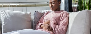 A person in a pink sweater sits uncomfortably on a couch, highlighting medbridge's role in enhancing home healthcare solutions.